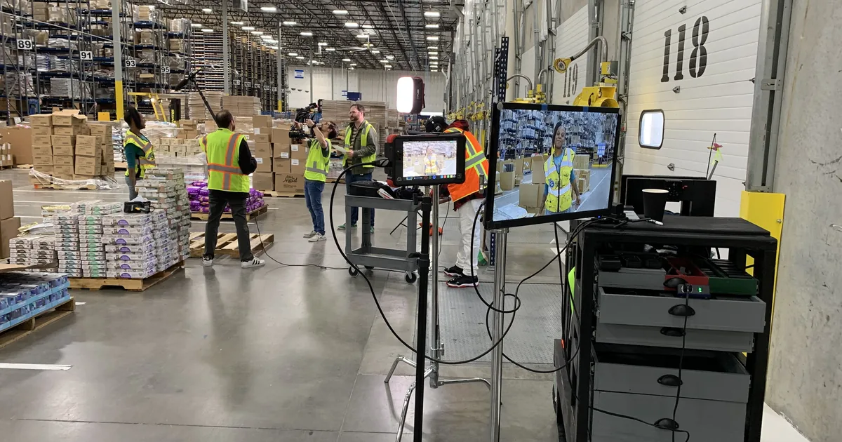 Production crew filming a presenter inside a Chewy fulfillment warehouse, with monitor playback in the foreground