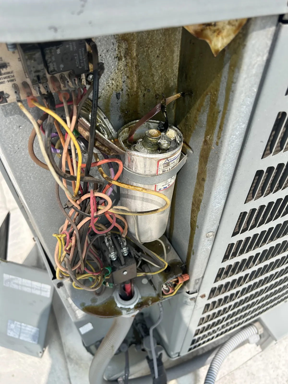 An outdoor condenser with its service panel off, showing a burnt capacitor and the control wiring inside.