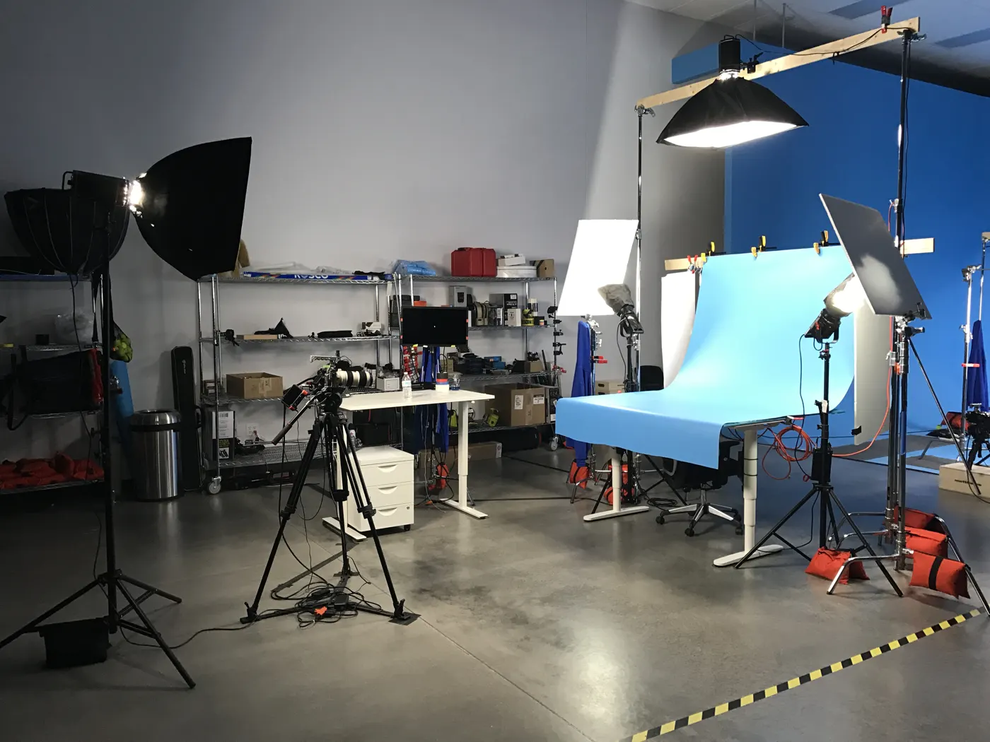 Product photography setup with a blue paper sweep, softbox lights and a camera on a tripod in a studio