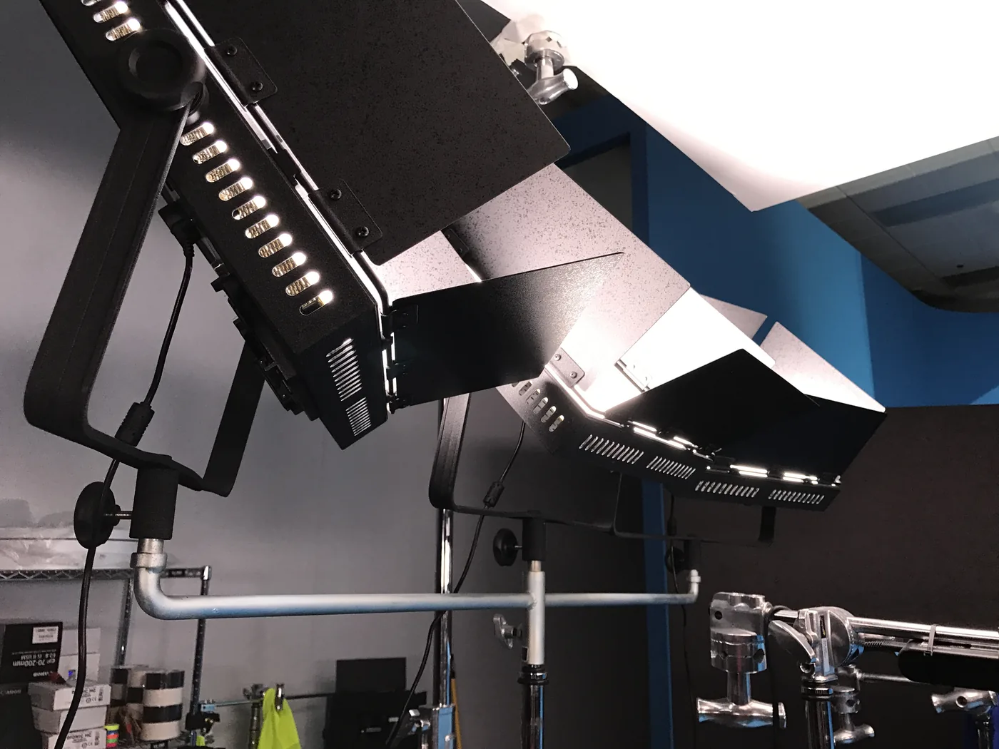 Close-up of studio light fixtures with barn doors, rigged on a pipe against a blue wall